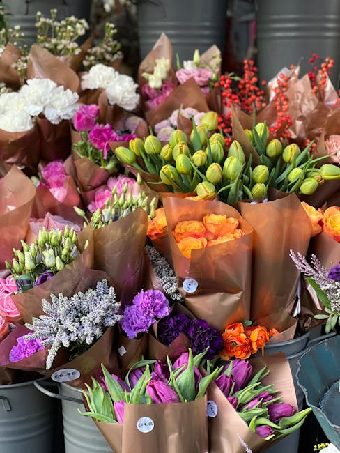 A vibrant collection of fresh flowers arranged in brown paper wrapping, showcasing a variety of blooms such as white hydrangeas, purple lisianthus, orange roses, pink tulips, green unopened tulip buds